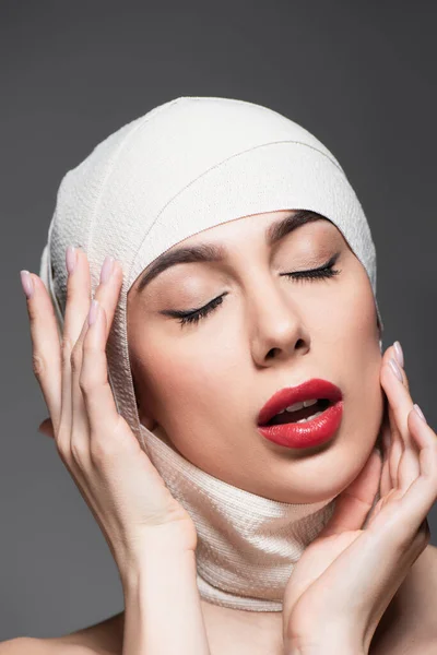 Jeune femme en bandage élastique sur la tête et lèvres rouges isolées sur gris — Photo de stock