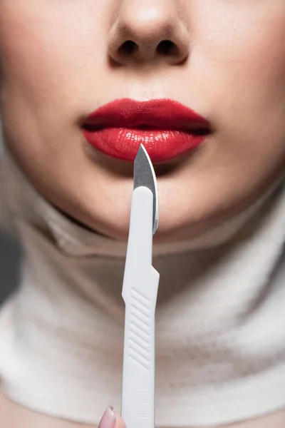 Vista recortada de mujer joven con labios rojos cerca de cuchillo quirúrgico afilado - foto de stock