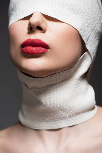 Close up of woman in elastic bandage with covered eyes and red lips isolated on grey — Stock Photo