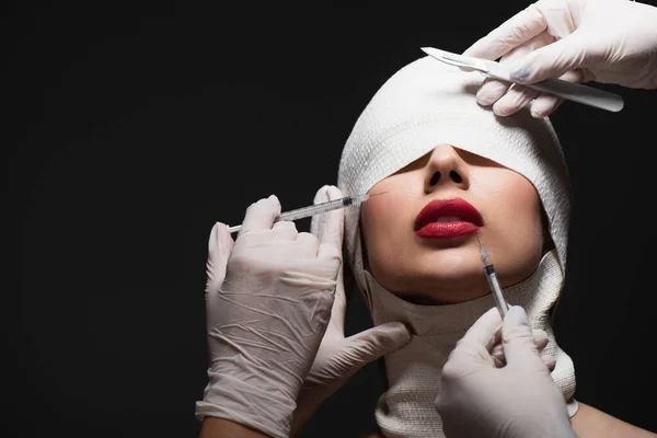 Jeune femme en bandage élastique près des chirurgiens plasticiens avec couteau chirurgical et seringues isolées sur gris — Photo de stock