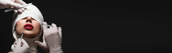 Femme en bandage élastique près des chirurgiens plasticiens avec couteau chirurgical et seringues isolées sur gris, bannière — Stock Photo