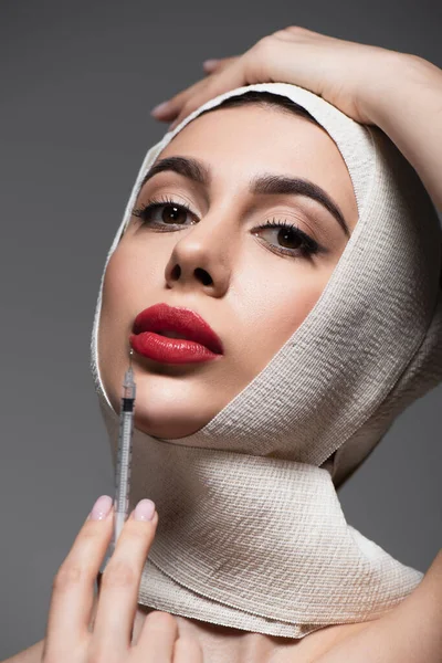 Young woman in elastic bandage on head holding syringe isolated on grey — Stock Photo