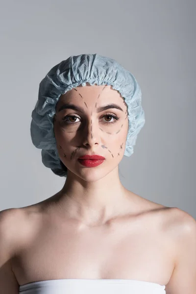 Mujer joven en gorra quirúrgica con líneas marcadas en la cara aislada en gris - foto de stock