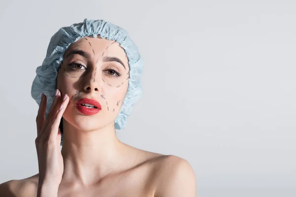 Young woman in surgical cap with bare shoulders and marked lines on face isolated on grey — Stock Photo