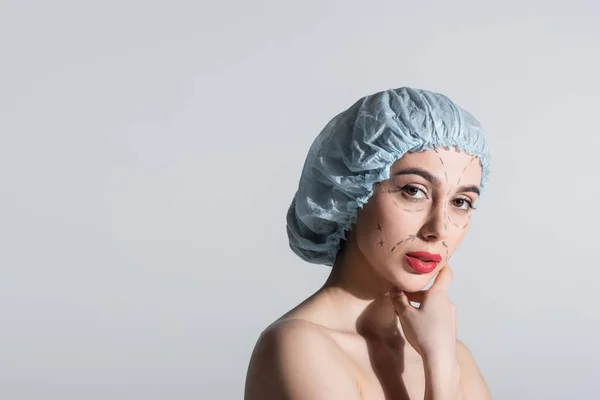 Mujer en gorra quirúrgica azul con hombros desnudos y líneas marcadas en la cara aisladas en gris - foto de stock