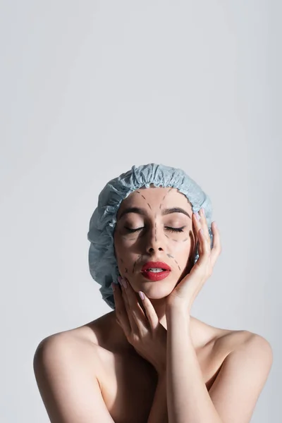 Молода жінка в хірургічній шапці торкається обличчя з поміченими лініями ізольовані на сірому — стокове фото
