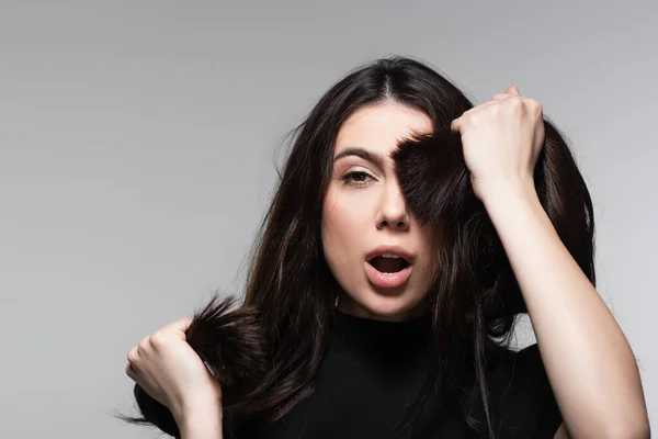 Shocked young woman covering eye with brown hair isolated on grey — Stock Photo