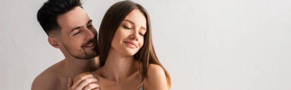 Young shirtless man hugging seductive woman smiling with closed eyes isolated on grey, banner — Foto stock