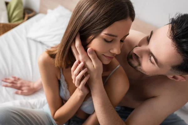 Молодий сексуальний чоловік торкається обличчя чуттєвої жінки, спокушаючи її в спальні — стокове фото