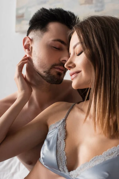 Sexy and tender woman in bra touching neck of young man with closed eyes - foto de stock