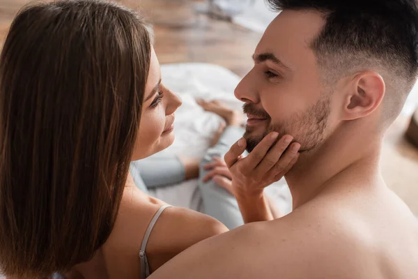 Young and tender woman touching face of young smiling man in bedroom — Foto stock