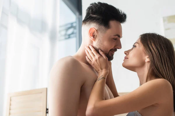 Happy young lovers looking at each other while standing face to face in bedroom — Stock Photo