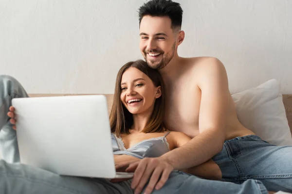 Joyful couple of lovers watching comedy film on blurred laptop in bed — стоковое фото