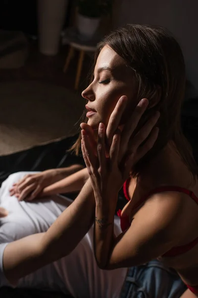 Sensual woman with closed eyes near man touching her face in bedroom at night — Stock Photo