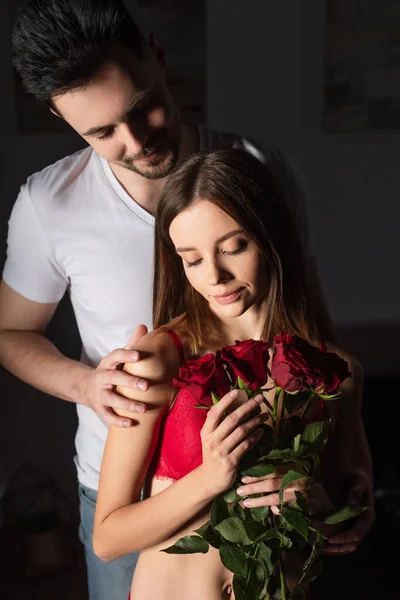 Hombre en camiseta blanca sonriendo cerca de la joven sexy mujer con rosas rojas - foto de stock