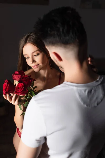 Back view of blurred man in white t-shirt presenting red roses to sensual smiling woman — Stock Photo