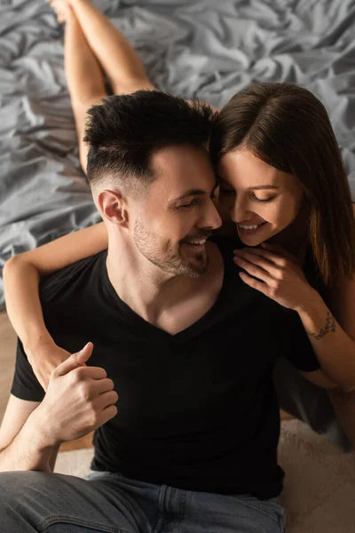 Vista de ángulo alto de la mujer joven y feliz abrazo sonriente hombre en camiseta negra en el dormitorio — Stock Photo