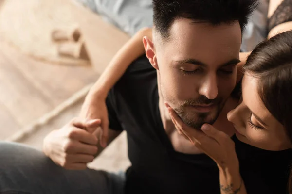 Overhead view of sensual woman touching face of man holding her hand in bedroom — Stock Photo