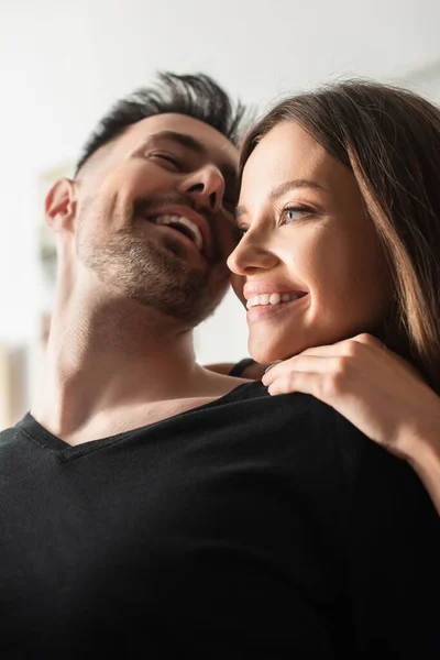 Low angle view of happy young woman embracing laughing boyfriend in bedroom — Fotografia de Stock