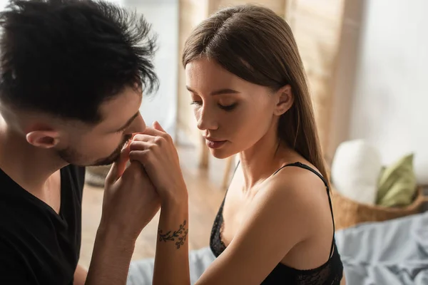 Blurred man kissing hand of tattooed woman in black bra in bedroom — Stock Photo