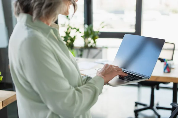 Ausgeschnittene Ansicht von Geschäftsfrau mittleren Alters mit Laptop mit leerem Bildschirm im Büro — Stockfoto