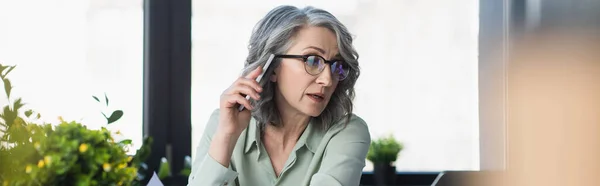 Зрелая деловая женщина разговаривает по мобильному телефону в офисе, баннер — стоковое фото