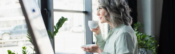 Vue latérale d'une femme d'affaires d'âge moyen tenant une tasse de café près d'un tableau à feuilles mobiles au bureau, bannière — Photo de stock