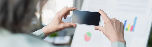 Vue recadrée de la femme d'affaires prenant des photos sur un téléphone mobile près de tableau à feuilles floues dans le bureau, bannière — Photo de stock