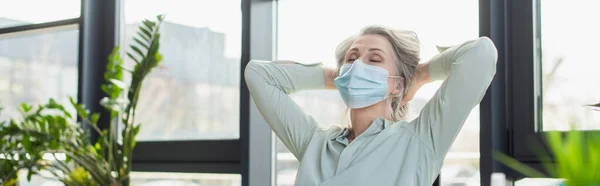 Grauhaarige Geschäftsfrau mit medizinischer Maske ruht im Büro, Banner — Stockfoto