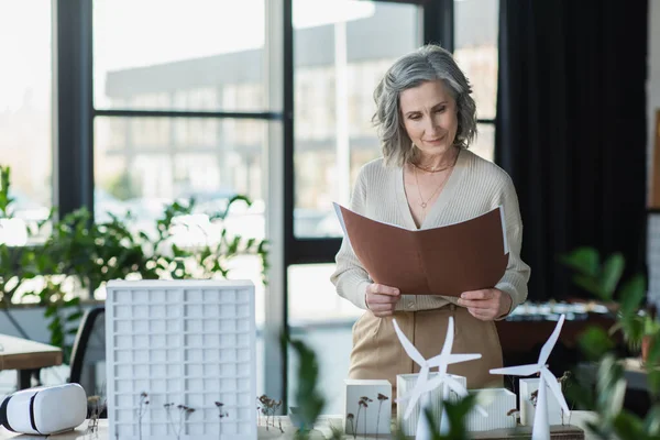 Businesswoman holding paper folder near models of buildings and vr headset in office — Stock Photo