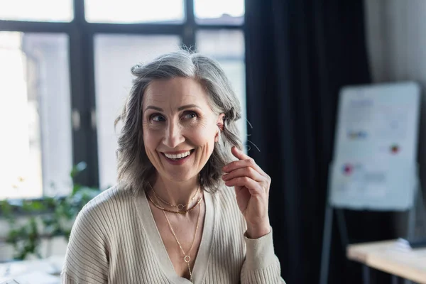 Grey haired businesswoman in earphone looking away in office — Stock Photo