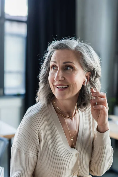 Sorridente donna d'affari matura utilizzando auricolare in ufficio — Foto stock