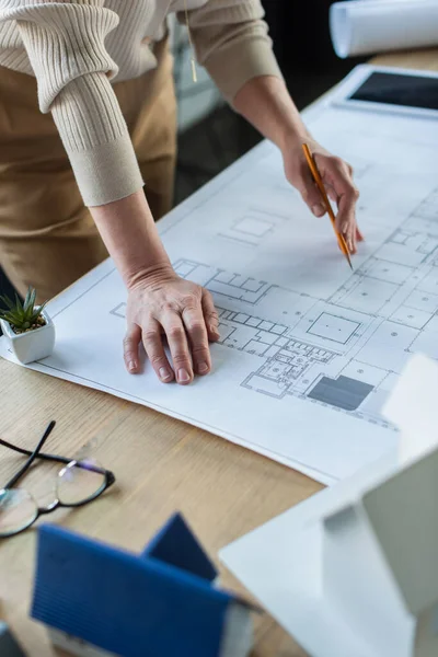 Cropped view of businesswoman holding pencil near blueprint and models of houses in office — Stock Photo