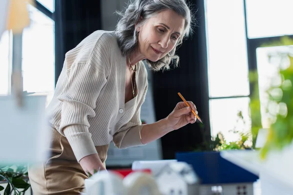 Geschäftsfrau hält Bleistift in der Nähe verschwommener Häusermodelle im Büro — Stockfoto