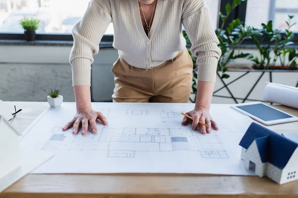 Cropped view of mature businesswoman holding pencil near blueprint and digital tablet in office — Stock Photo