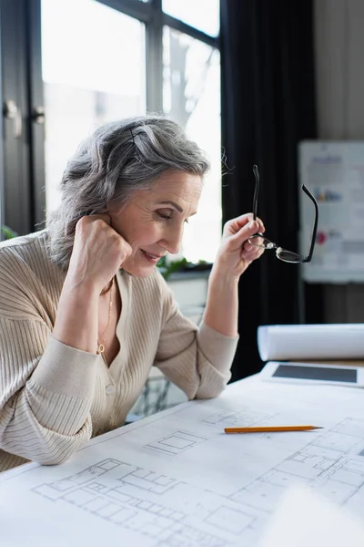 Positive Geschäftsfrau mit Brille in der Nähe von Blaupause im Amt — Stockfoto