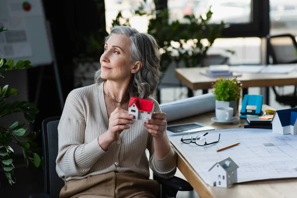 Businesswoman holding model of house near eyeglasses and blueprint in office — Stock Photo