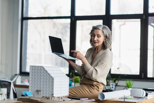 Geschäftsfrau mit Videoanruf auf Laptop in der Nähe von Blaupause und Modell des Bürogebäudes — Stockfoto