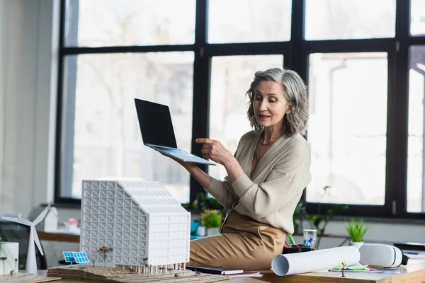 Femme d'affaires ayant appel vidéo sur ordinateur portable près du plan directeur et modèle de bâtiment dans le bureau — Photo de stock