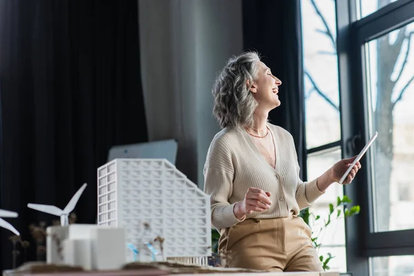 Seitenansicht positiver Geschäftsfrau mit digitalem Tablet in der Nähe von Modellen von Bürogebäuden — Stockfoto