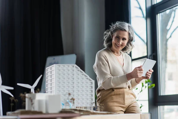 Businesswoman holding digital tablet near models of buildings in office — Stock Photo