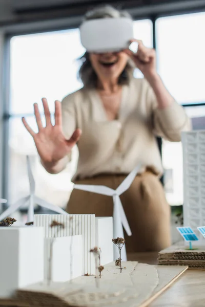 Modelli di edifici vicino a donna d'affari offuscata in cuffia vr in ufficio — Stock Photo