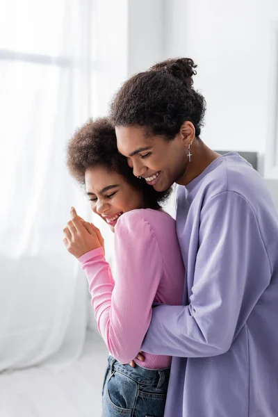 Positiver afrikanisch-amerikanischer Mann umarmt Freundin zu Hause mit geschlossenen Augen — Stockfoto