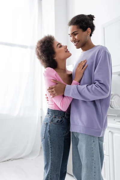 Positiv afrikanisch-amerikanisches Paar schaut einander an, während es sich zu Hause umarmt — Stockfoto