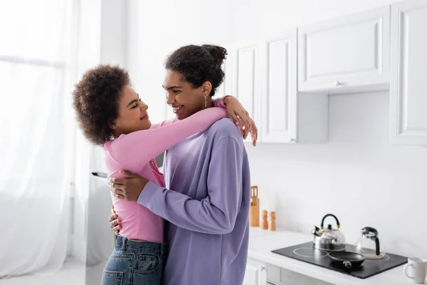 Africano americano hombre abrazando joven novia en cocina - foto de stock