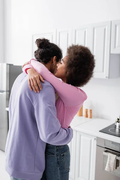 Mujer afroamericana abrazando y susurrando a su novio en casa - foto de stock