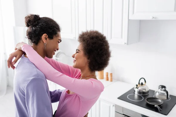 Vista lateral da mulher afro-americana abraçando o jovem na cozinha — Fotografia de Stock