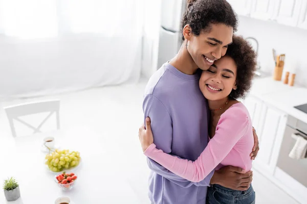 Giovane coppia afro-americana che si abbraccia vicino ai frutti in cucina — Foto stock