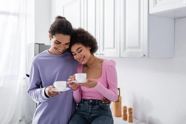 Cheerful african american couple holding cups in kitchen — Stock Photo