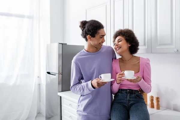 Positiva pareja afroamericana sosteniendo tazas de café en la cocina - foto de stock